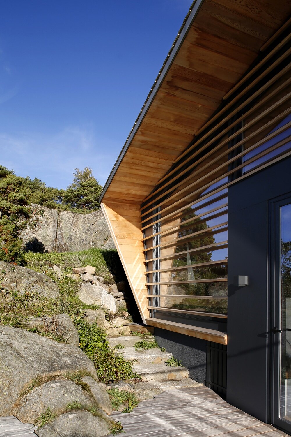 Modern contrasting facade with wooden louvers on a rocky site