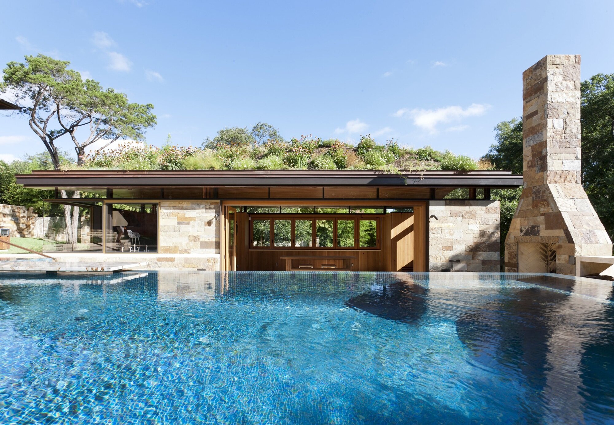 Eco-friendly facade with green roof: harmony of stone, wood and glass by the water