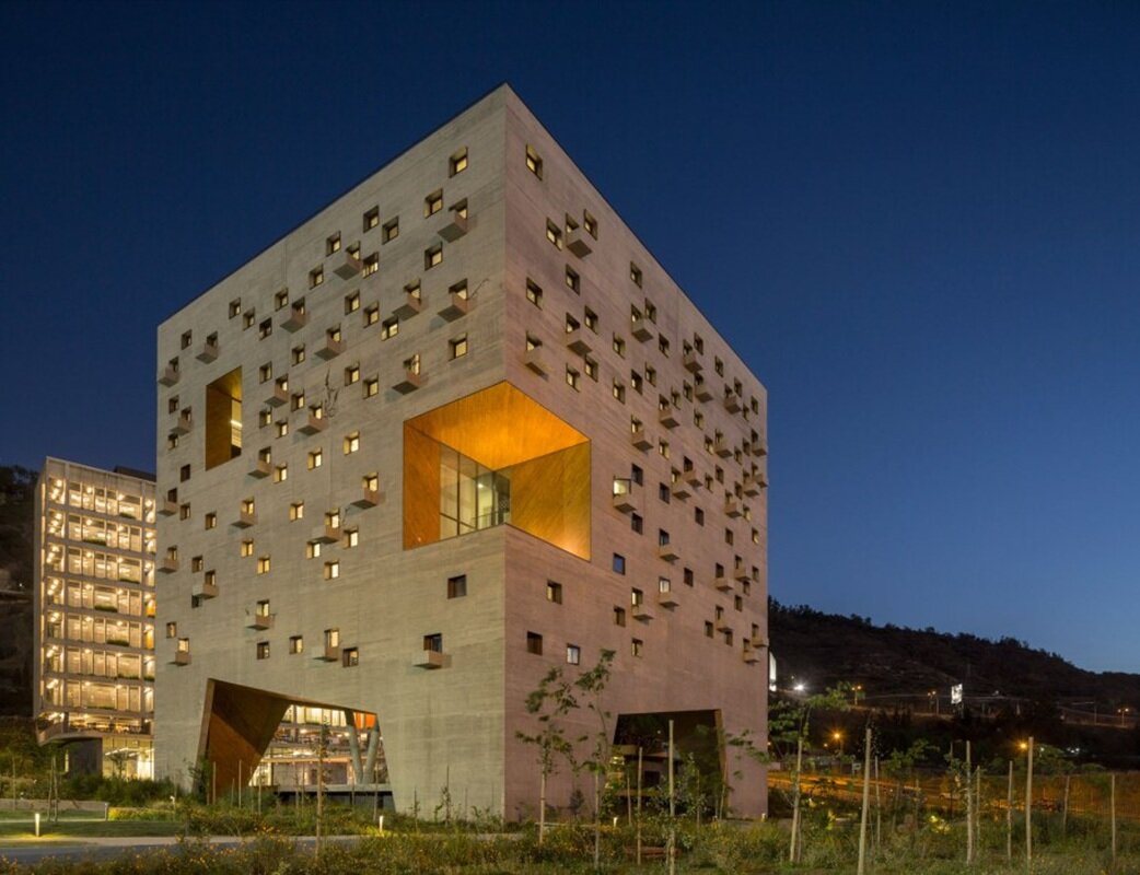 Cubic perforated facade: illuminated concrete cube with orange niches