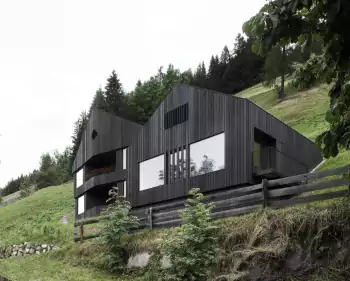 Modern mountain house with dark wooden facade and contrasting window openings