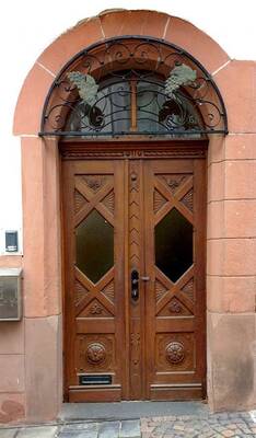 Traditional European double door in an arched opening with artistic ironwork elements on a pink sandstone facade