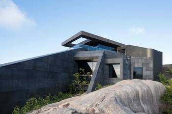 Brutalist Facade: Modern Stone-Clad House on Rocky Landscape